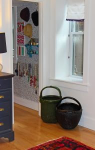 A picture of the outside of the closet. There is a blue chest of drawers and a couple of Chinese water baskets under a window sitting outside of the closet