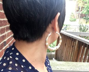 A picture of a woman with short dark hair. It is the back of her head. She is wearing a pair of gold, bone, door knocker, hoop earrings