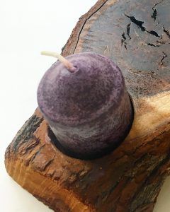 A small purple tea candle in a wooden candle holder