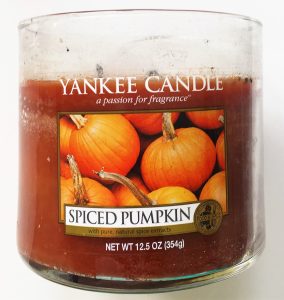 A picture of an orange candle in a glass, cylinder container. On the front there is a label saying Yankee Candle with a picture of pumpkins and the words "Spiced Pumpkin" on it. 