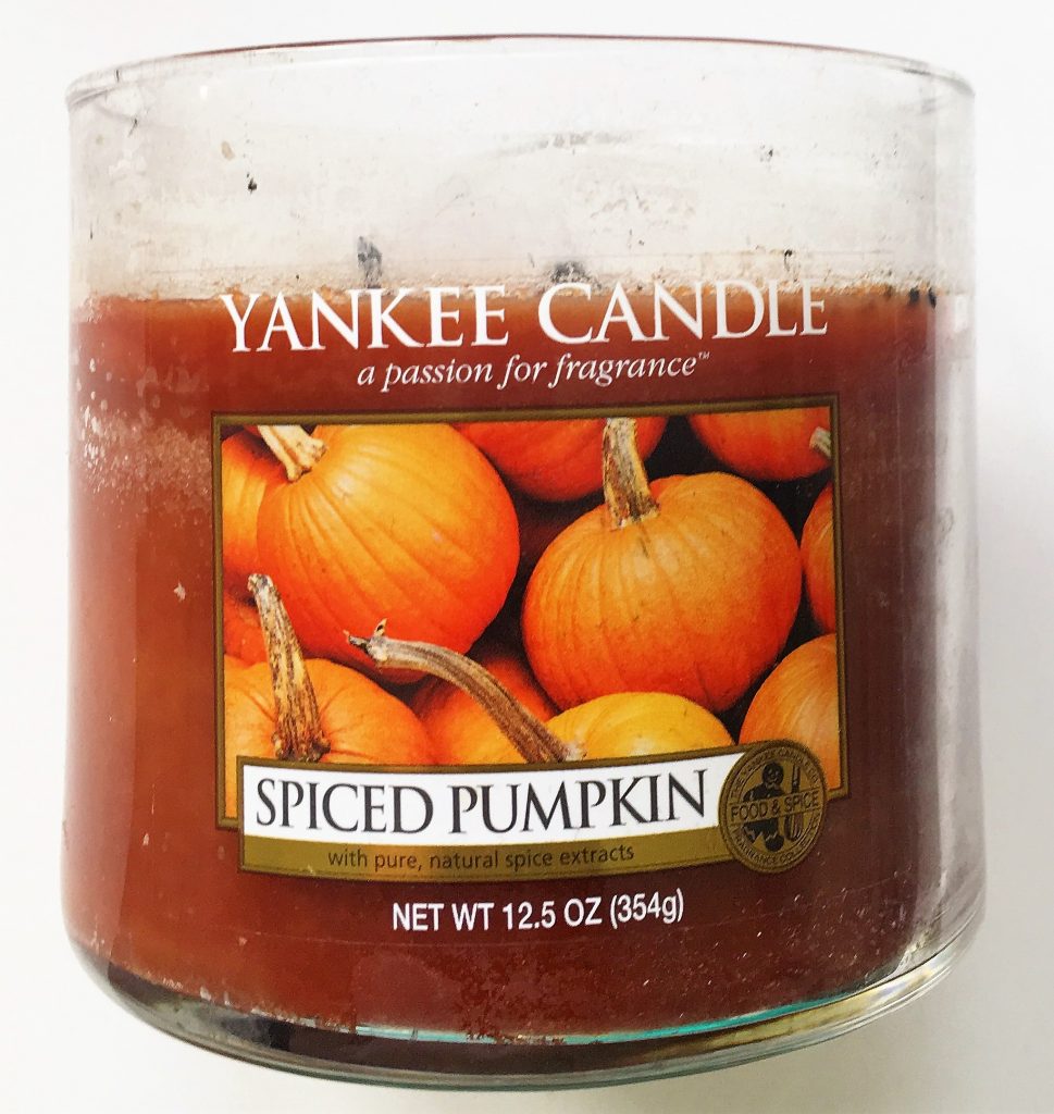 A picture of an orange candle in a glass, cylinder container. On the front there is a label saying Yankee Candle with a picture of pumpkins and the words "Spiced Pumpkin" on it.