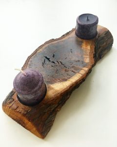 Two small purple tea candles on either end of a larger wooden natural looking candle holder