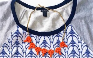 A close up of the salmon colored baulb necklace against the J Crew top