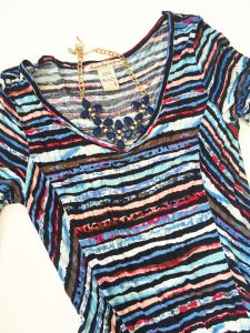 A picture of the top of a high-low dress with watercolors like pink, blue, purple and black print in a size large. Also pictured is a blue, bulb necklace 