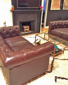 A picture of a living room with leather couches, a coffee table with a frame and glass top, a fireplace, and a white carpet