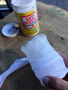 A picture of a vase being wrapped in gauze using mod podge. You can see the mod podge in the background