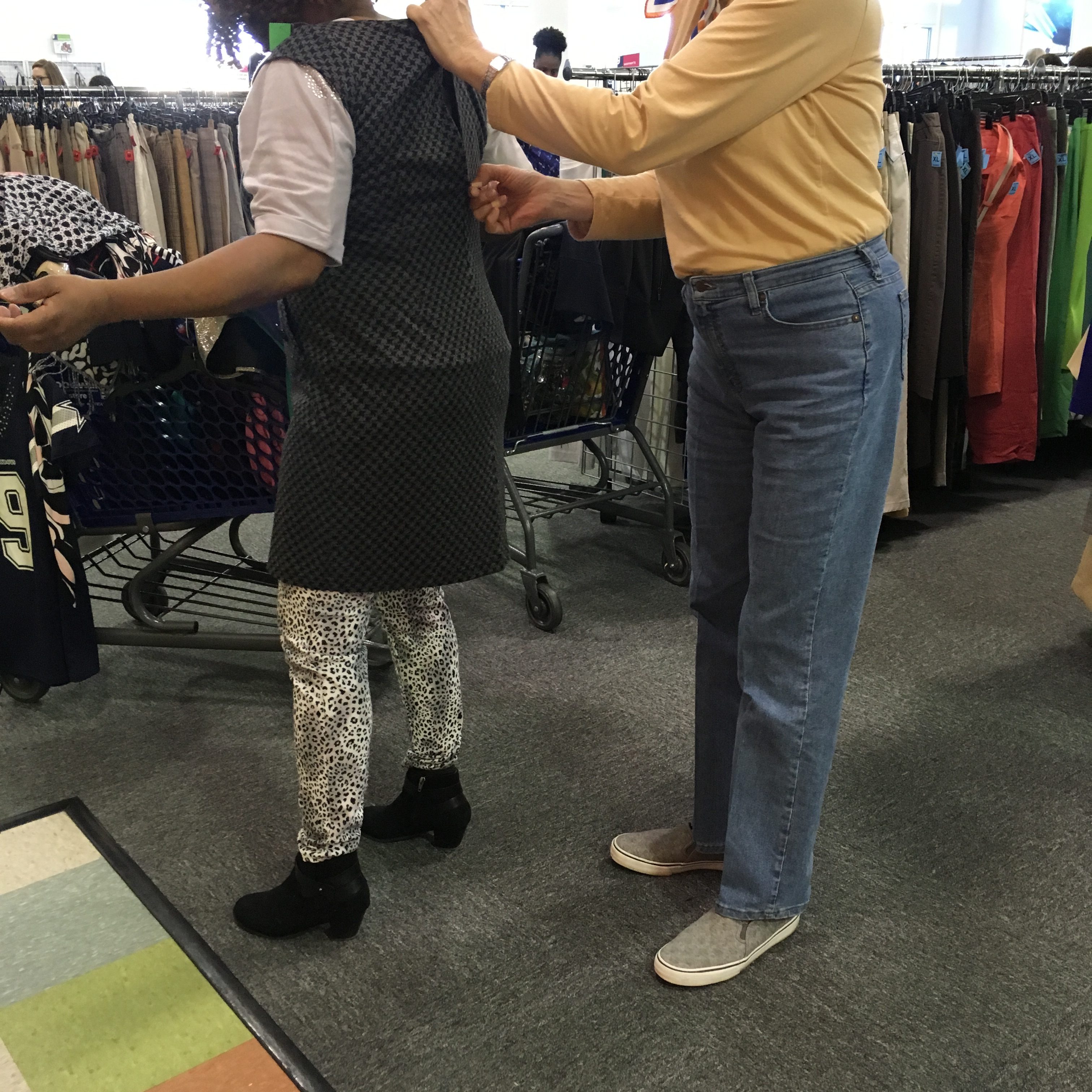 Goodwill shopper helping another Goodwill shopper zip dress