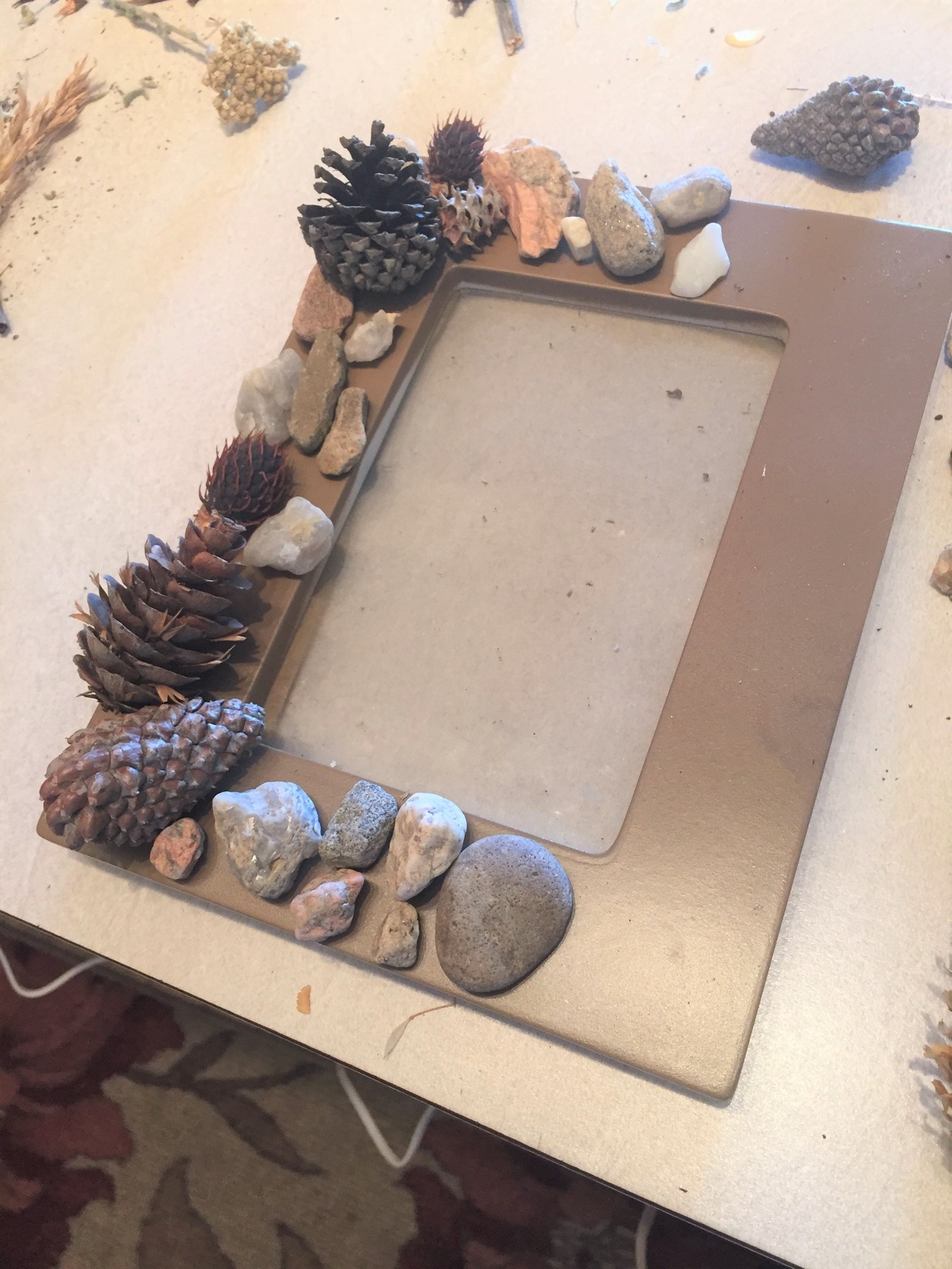 Tim uses assorted rocks, pebbles, and pine cones to decorate a painted picture frame.