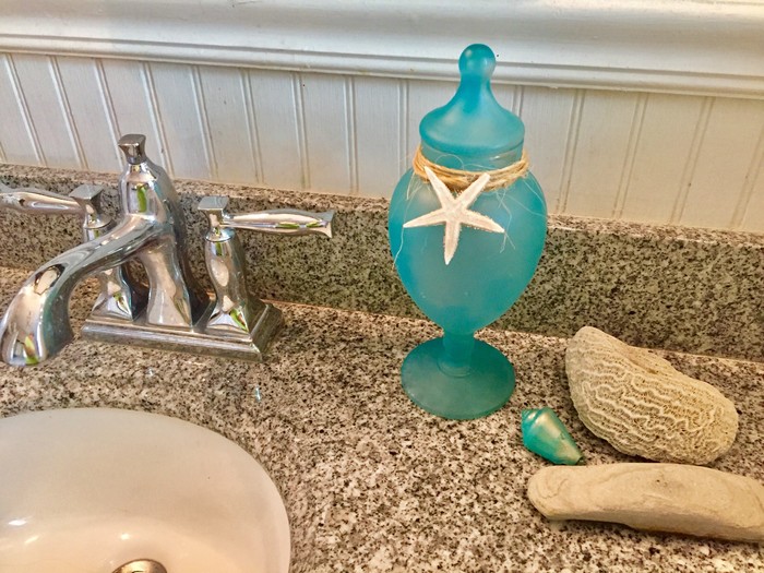 Tim's sea glass painted decanter along side some seashells and corral next to a bathroom sink