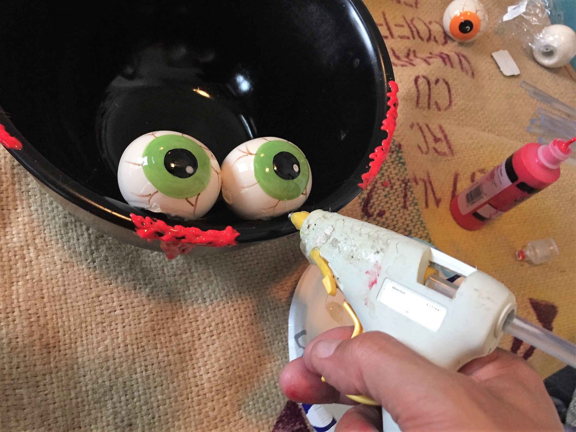 Tim secures spooky eyeballs to painted bowl with hot glue gun.