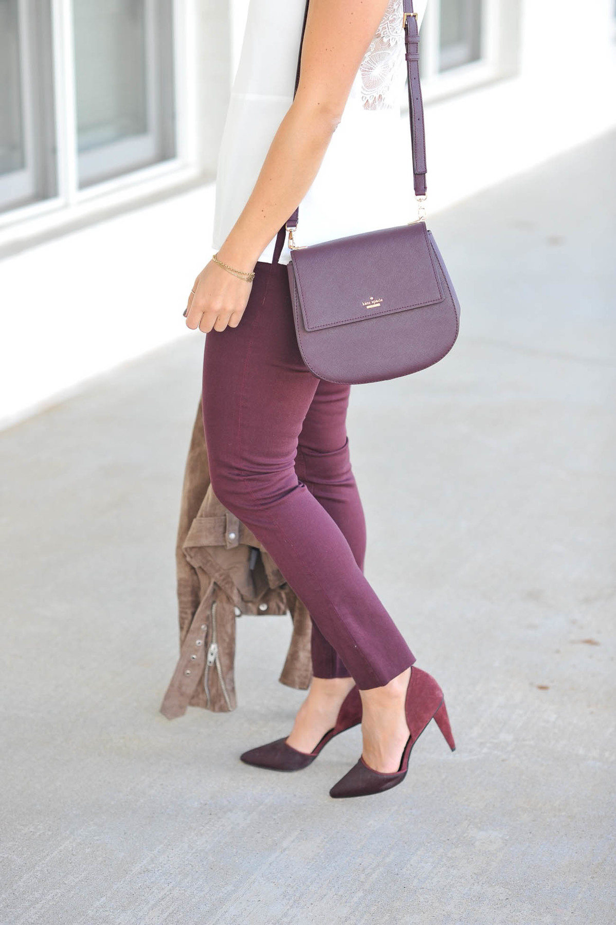 Model wears plum Kate Spade bag and matching plum pants and shoes.